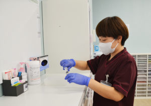 えんじ色のユニフォームを着用した看護師の画像です。透析中の注射薬を準備しています。